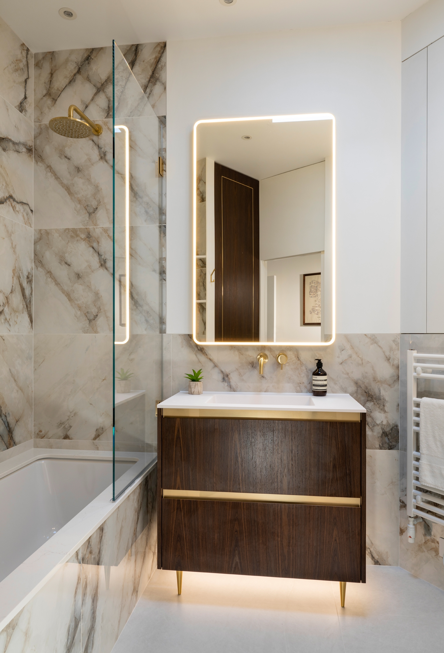 Luxurious bathroom with marble walls, a modern vanity, and backlit mirror
